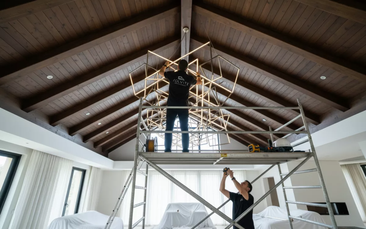 Installation de luminaire architectural sur mesure par Solvite Techniciens Solvite installant un lustre géométrique sur mesure dans une villa moderne avec plafond en bois apparent